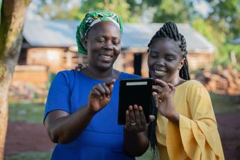 Two women consult a tablet computer, smiling.