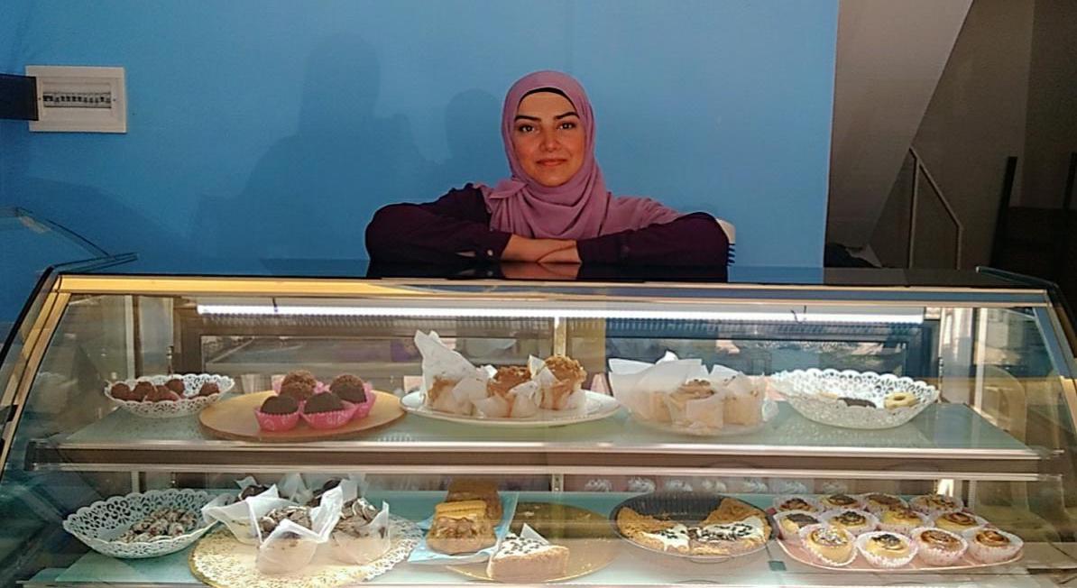 A business owner leaning on a display case of baked goods.