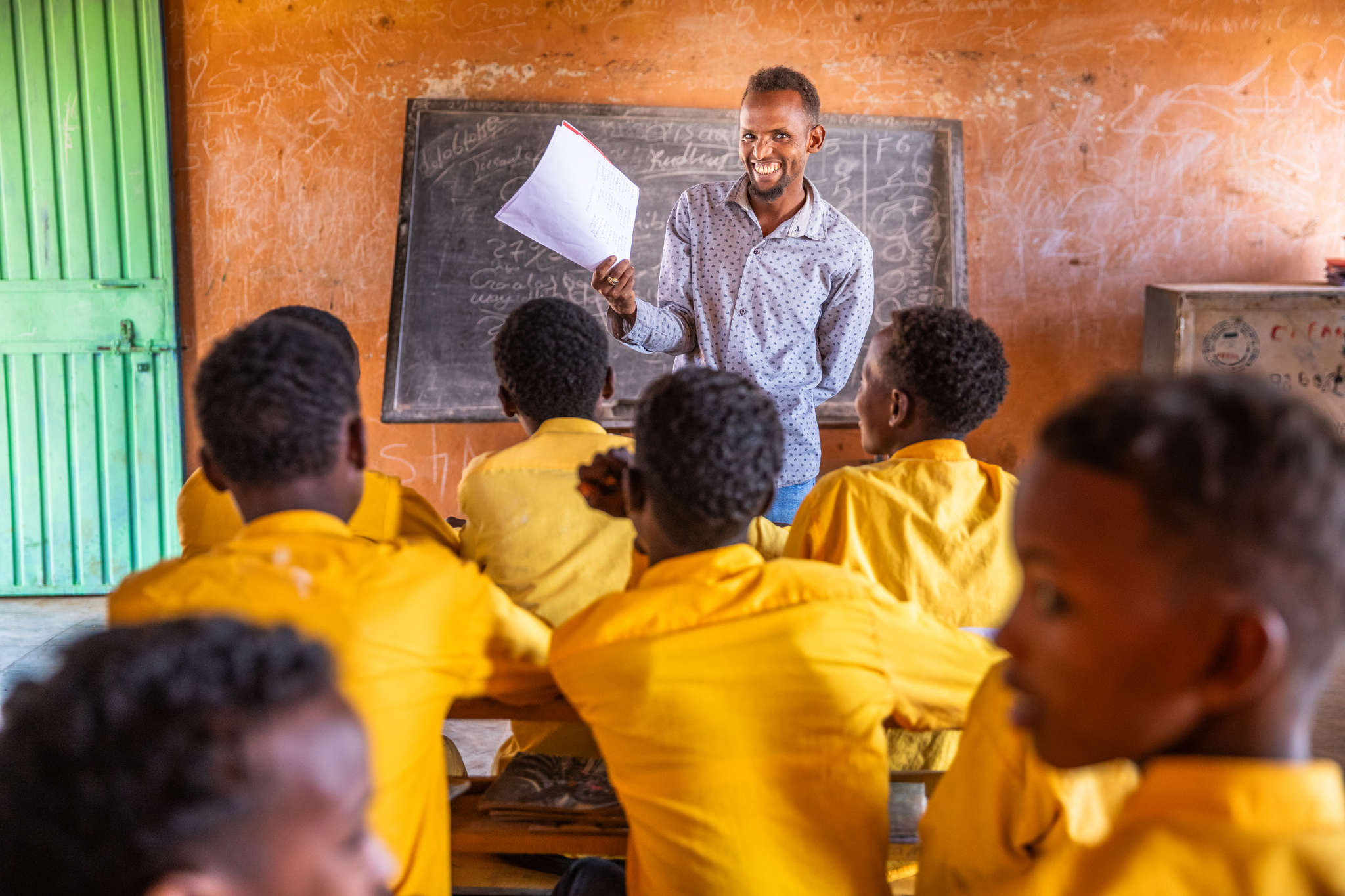 An adult teacher smiling at a classroom of young students.