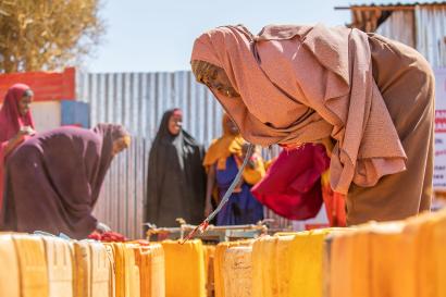 A woman crouches over water cans in Somalia