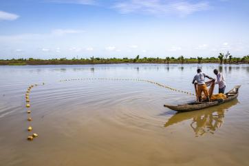 Two adults stand on a boat casting fishing nets on a river in nigeria.