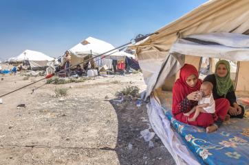 A person feeds a baby in a tent at a refugee camp.