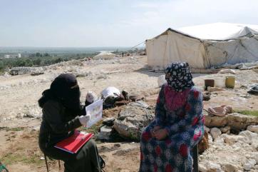 A person instructs a refugee outdoors. 