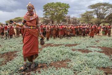 A woman pours a bit of water on weeds, symbolizing a request for rainfall.