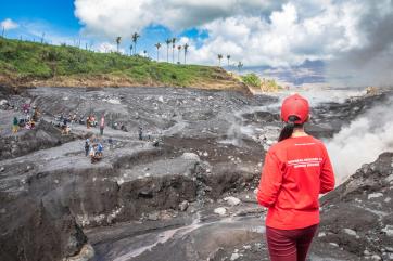 A person overlooking a village covered in ash after a nearby volcano erupted.