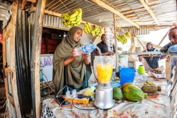 A vendor filing a blender with fruit and water at their food shop.