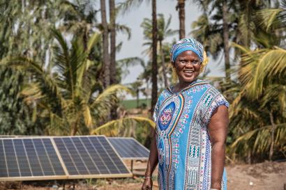 A farmer stands next to solar panels.