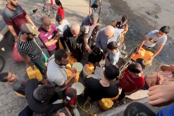 Caption: adults and children wait for hours at a public tap to fill containers with drinking water. photo by ©shadow pro for mercy corps.