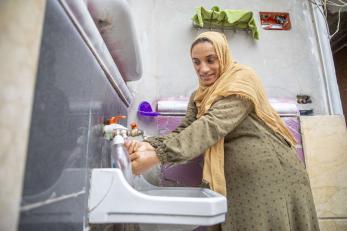 A woman washs her hands at a sink.