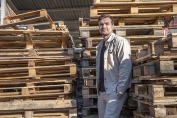 A young man stands aside some pallets