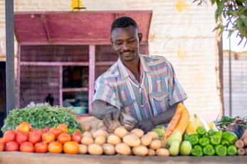 A man stands outside a fresh produce stall.