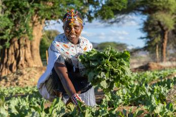 A woman in kenya smiles while harvesting greens