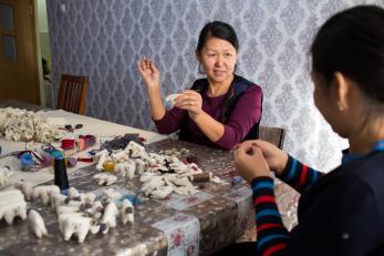 Women at a table sewing small felted rams