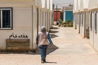 A person wearing a mercy corps vest walks between buildings in zaatari refugee camp, jordan.