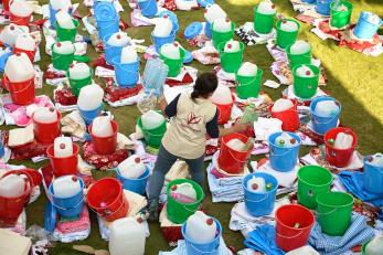 A Mercy Corps team member standing among buckets filled with emergency supplies in Nepal